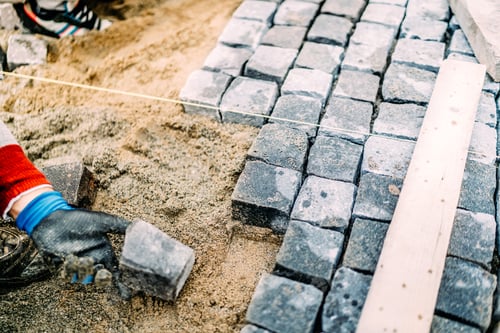 Preview: Close up of mason hands using granite stones to create pavement