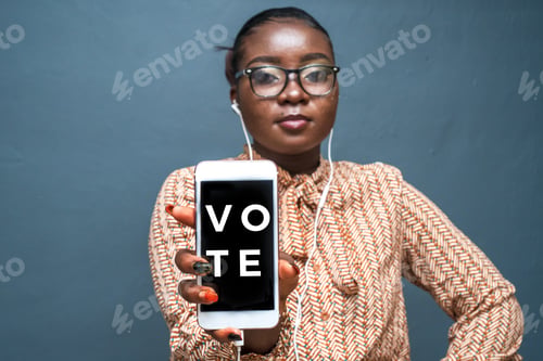 Preview: Closeup shot of a young lady wearing headphones holding her phone with writing "Vote"