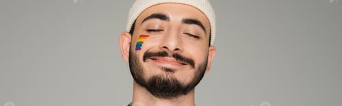 Preview: Smiling homosexual man in hat with lgbt flag on cheek isolated on grey, banner