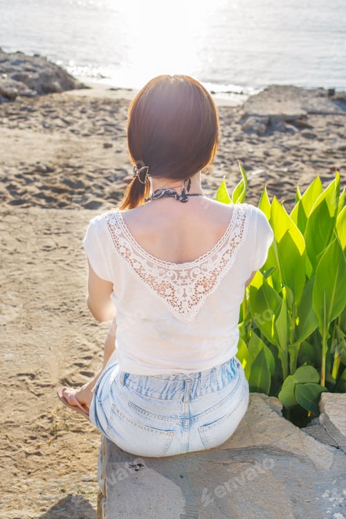 Preview: back view of a girl sitting on the sandy beach alone on the sea background