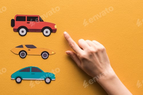Preview: cropped view of woman pointing with finger at paper cars on orange background