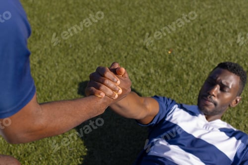 Preview: Two African American male athletes train on a field, one assists the other to stand