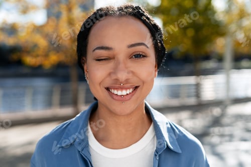 Preview: Young woman winking smiling outdoors with piercings