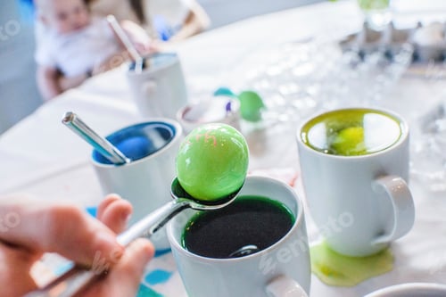 Preview: Close up of boy's hand removing green dyed egg from mug on table for Easter