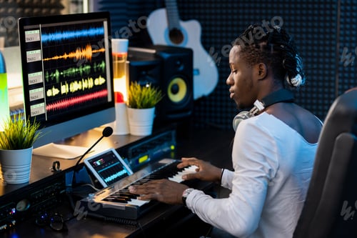 Preview: Serious young African man pressing keys of piano keyboard in sound record studio