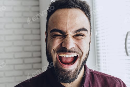 Preview: Smiling man laughs in front of a bright window during daytime activity