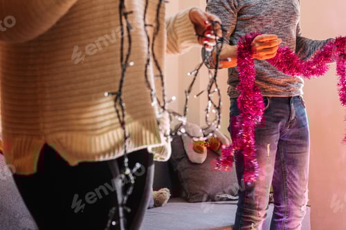 Preview: Unrecognizable couple decorating christmas tree with lights, holding glowing ribbons and decorations