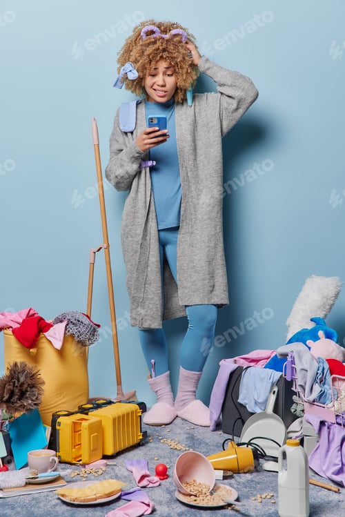 Preview: Puzzled confused housewife scratches head looks with dissatified expression at screen of smartphone