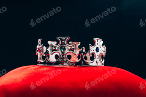 Preview: ancient silver crown with gemstones on red pillow, isolated on black