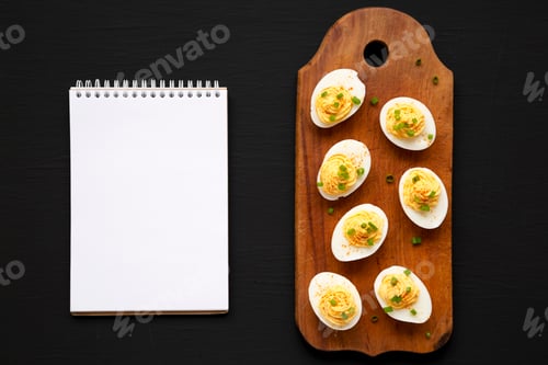 Preview: Homemade Deviled Eggs with Chives, blank notepad on a rustic wooden board on a black surface