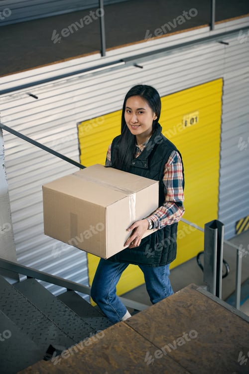 Preview: Joyous young storehouse worker carrying cargo upstairs
