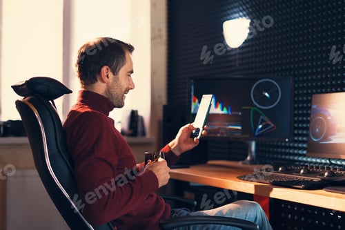 Vorschau: Junger Mann arbeitet im Studio mit Smartphone und Computer.