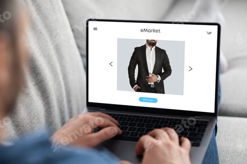 Preview: Young man choosing new suit on laptop screen, enjoy online shopping remotely from home, sitting on