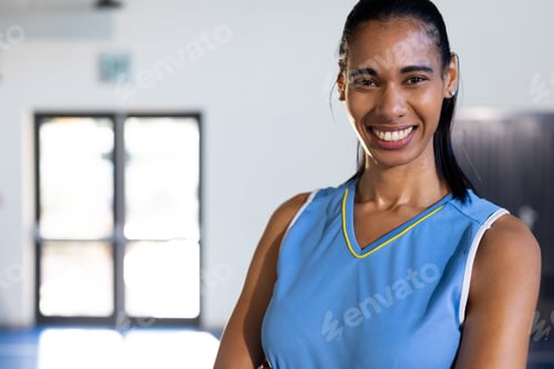 Preview: Smiling female basketball player in blue jersey posing confidently in gym
