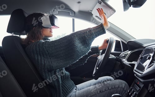 Preview: Side view of woman in virtual reality glasses that sitting inside of modern car