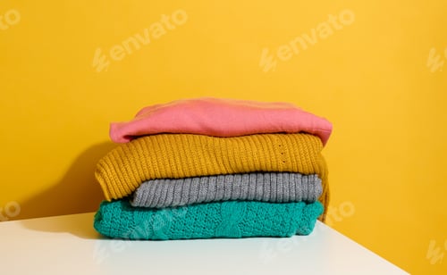 Preview: Stack of folded knitted sweaters on yellow background. Comfortable clothes