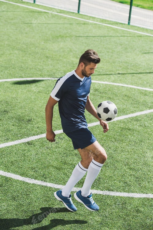 Preview: side view of soccer player kicking ball while training on soccer pitch