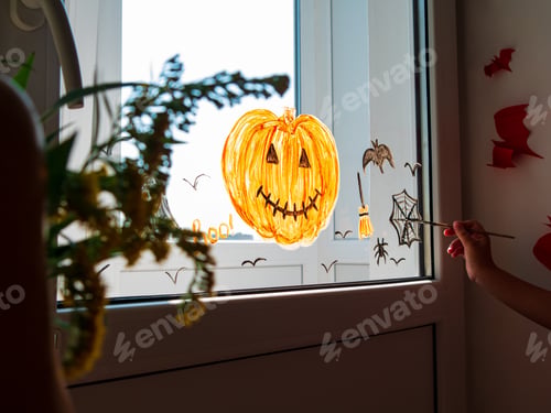 Preview: Child painting pumpkin on window preparing to celebrate Halloween. Little girl draws decorates