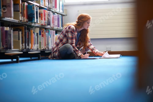 Preview: Young female college student writing notes on library floor