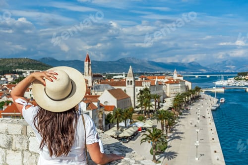 Preview: Rear view of woman standing on city walls looking at idyllic seaside town of Trogir, Croatia