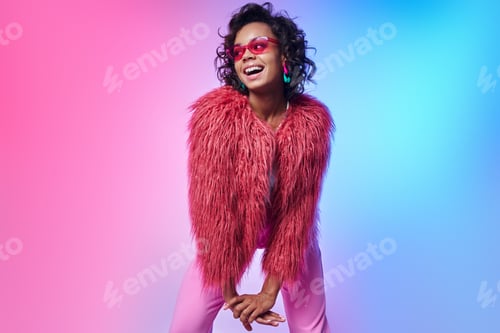 Preview: Happy African woman in fluffy jacket standing against colorful background
