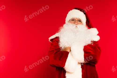 Preview: Bearded santa claus crossing arms and looking at camera on red background