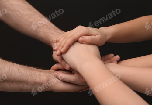 Preview: Young people putting their hands together on dark background, closeup