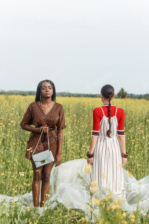 Preview: Black and white girls are standing opposite each other in a field with yellow flowers.
