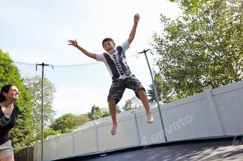 Preview: Mother watches son jumping on trampoline in garden
