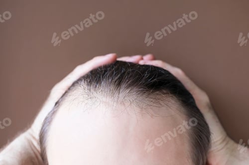 Preview: Man touching her hair close-up on brown background, hair loss concept.