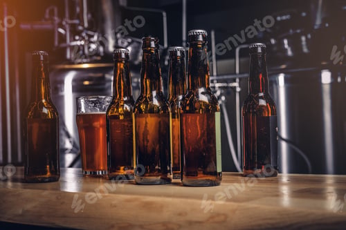 Vista previa: Bottles and glass of craft beer on wooden bar counter at the indie brewery.