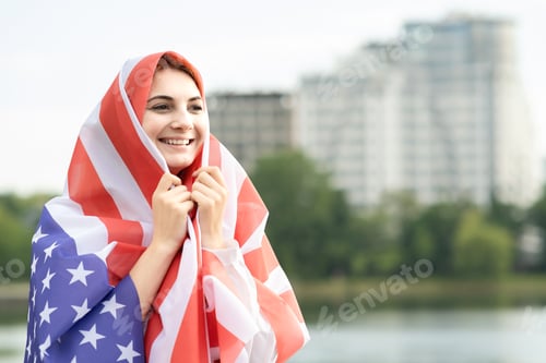 Preview: Portrait of young happy refugee woman with USA national flag on her head