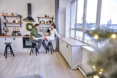 Preview: Loving couple in knitted sweaters hugging in fashionable kitchen in stylish interior. Christmas
