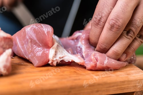 Preview: Closeup shot of hands cutting the raw meat with a sharp knife