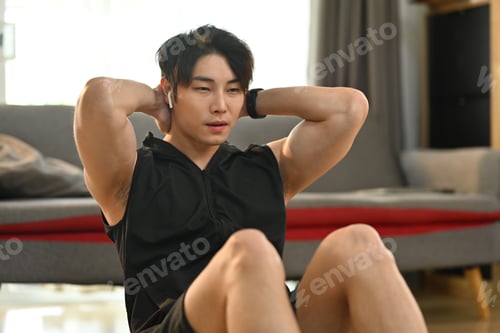 Preview: Fit muscular asian man doing abdominal sit ups in living room.