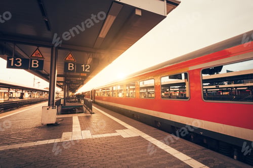 Preview: Beautiful railway station with modern red commuter train at suns