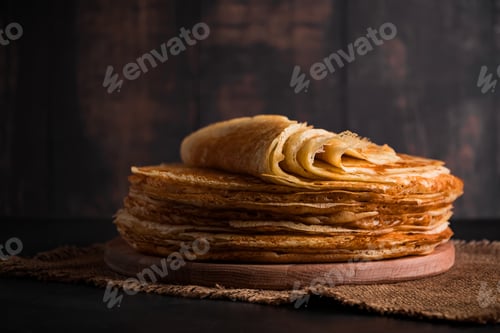 Preview: A stack of thin pancakes on a dark wooden background.