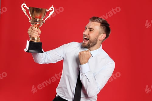 Preview: Portrait of happy young businessman with gold trophy cup on red background