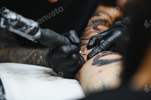 Preview: tattooist with his machine tattooing on the arm with the design drawn, concept of art and design