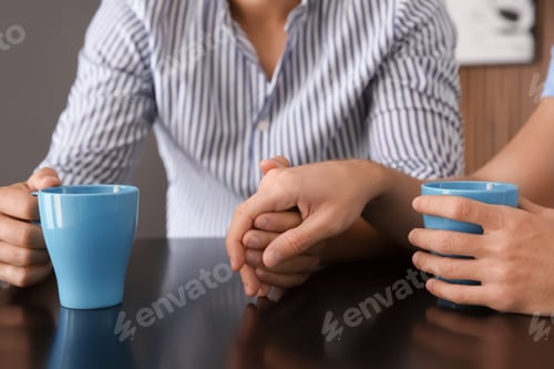 Preview: Happy gay couple with coffee at table indoors, closeup