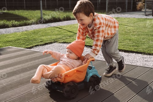 Preview: Brother giving a ride to baby sister in big toy car in yard