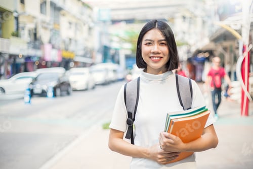 Preview: Smiling young asian woman with her book backpack in the city