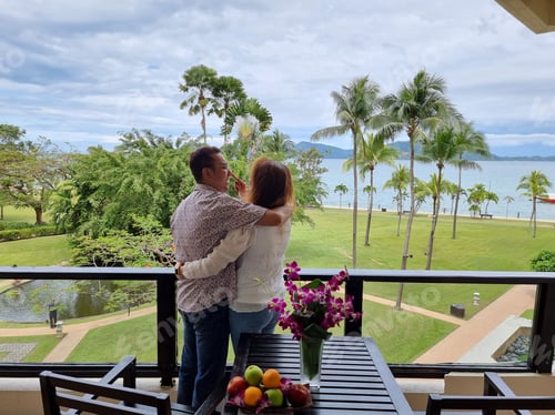 Couple Embracing on Balcony Overlooking Lush Tropical Beach