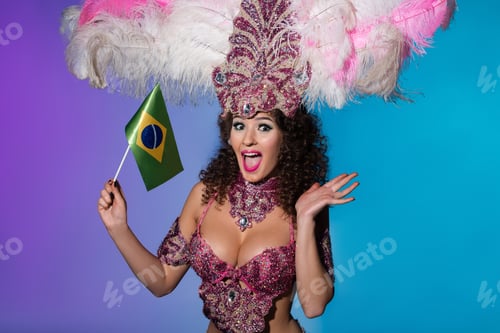 Preview: Cheerful woman in carnival costume with pink feathers holding flag of Brasil isolated on blue