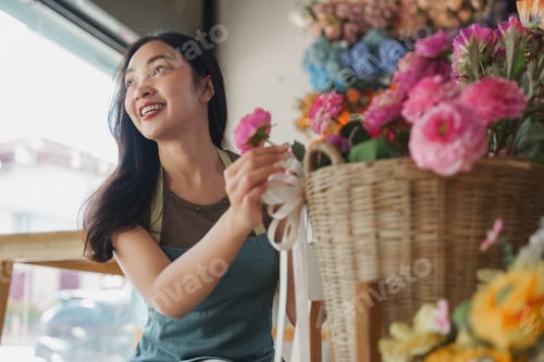 Preview: Young woman florist arranging flowers in shop