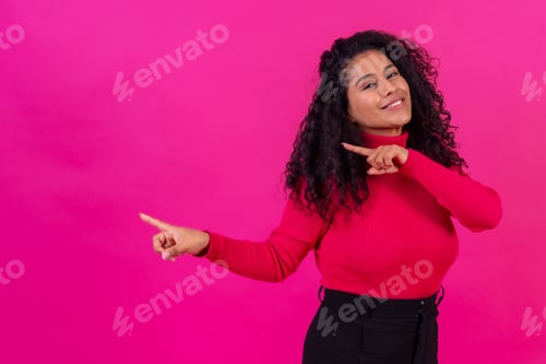Preview: Curly-haired woman pointing left on a pink background, studio shot, copy paste