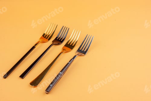 Preview: Top view of elegant shiny stainless forks on the right side on isolated golden background with free