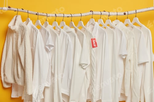 Preview: Clearance sale of white clothes on hangers isolated over yellow background. Selection of fashion gar