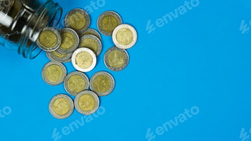 Preview: Coins Spill from Glass Jar on Blue Surface