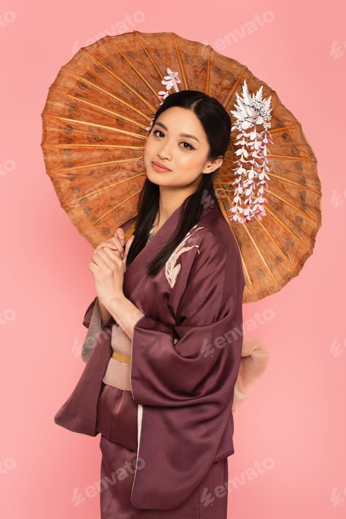 Preview: Japanese woman with umbrella looking at camera isolated on pink